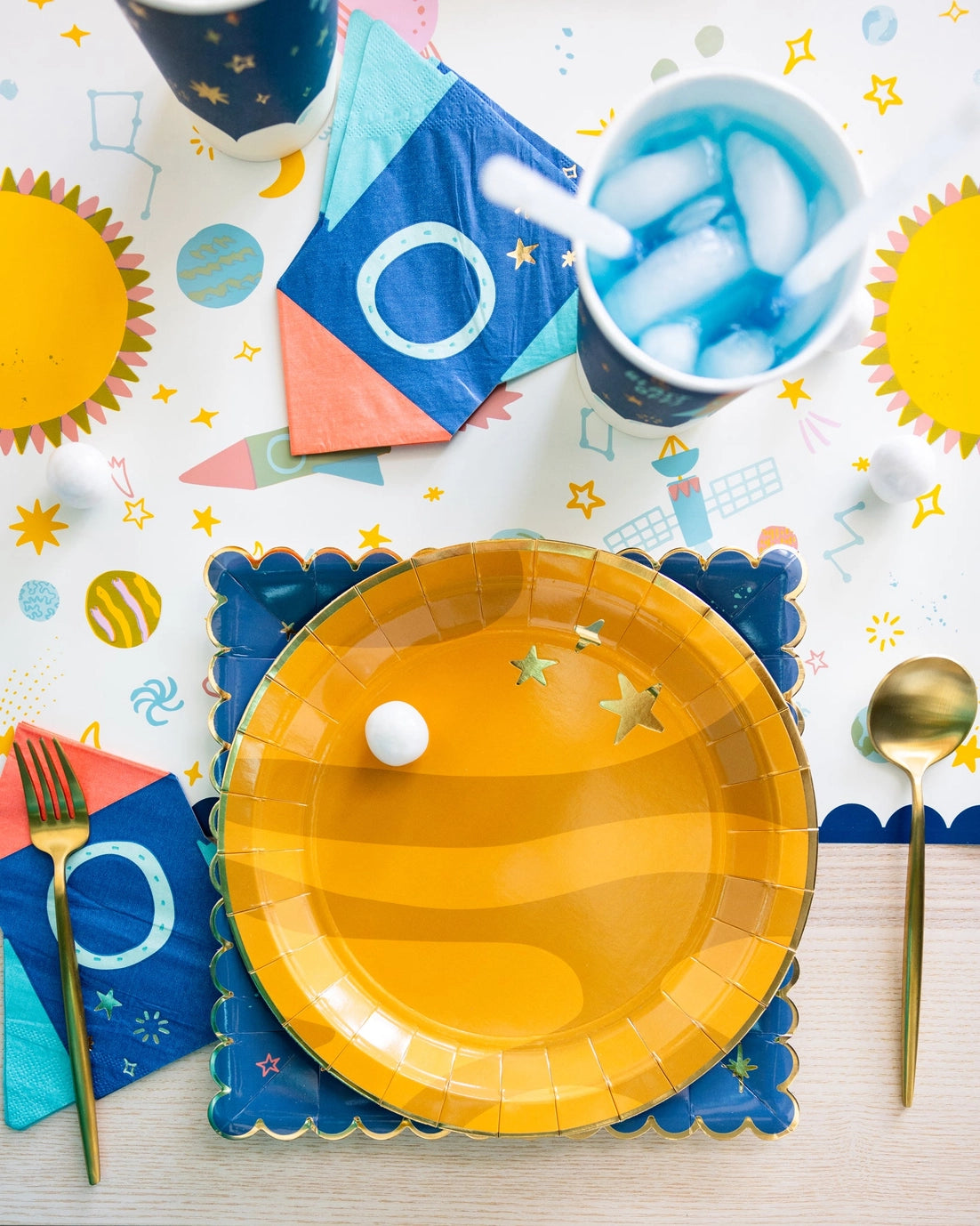 Yellow paper plate with a white ball on a colorful table setting with cups, napkins, and utensils.