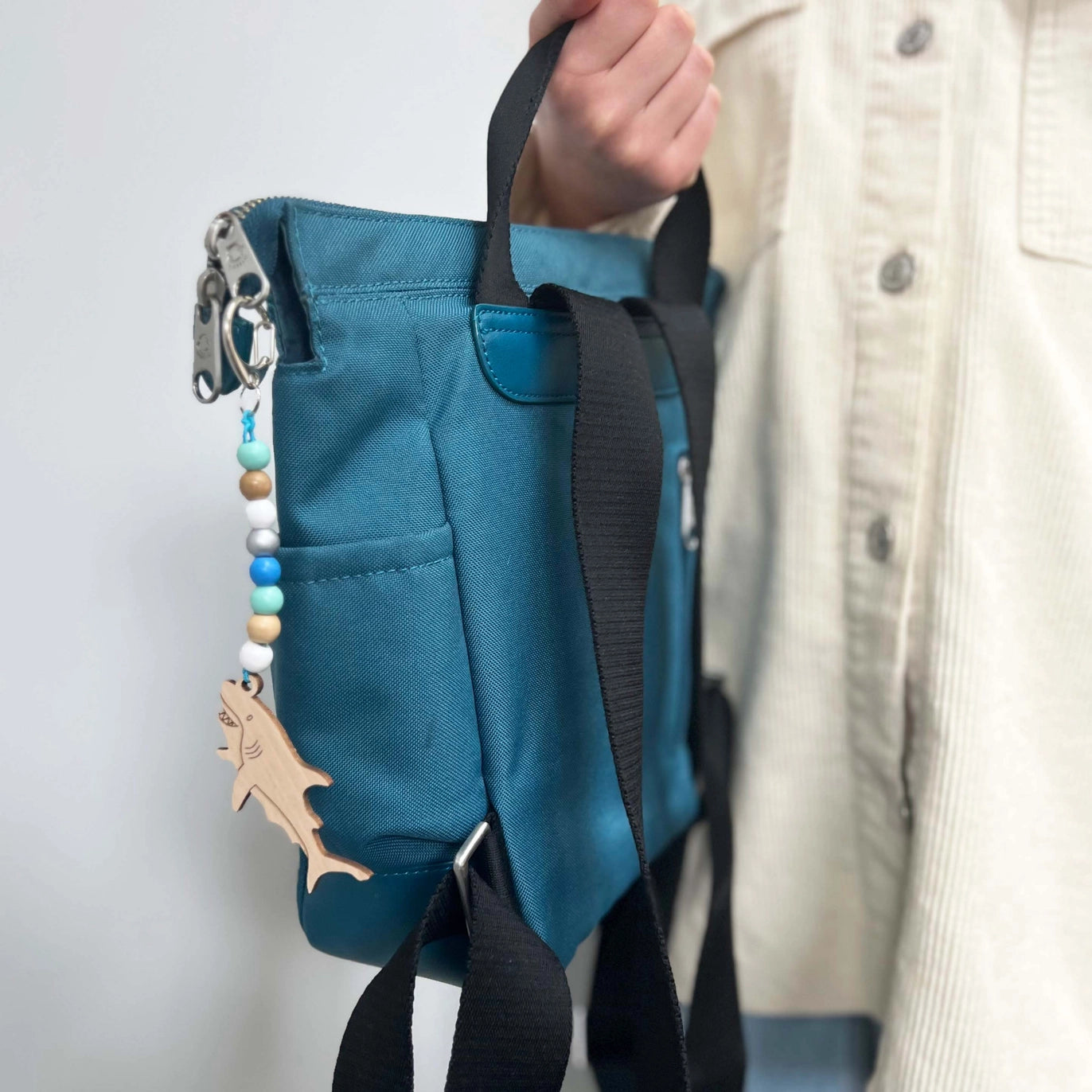 Blue bag with a shark keychain attached, held by a person wearing a beige jacket.