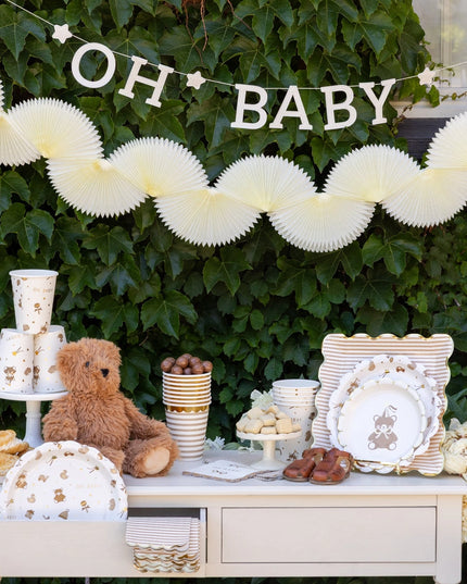 Baby shower setup with 'OH BABY' banner, teddy bear, and decorative items against a green leafy background.
