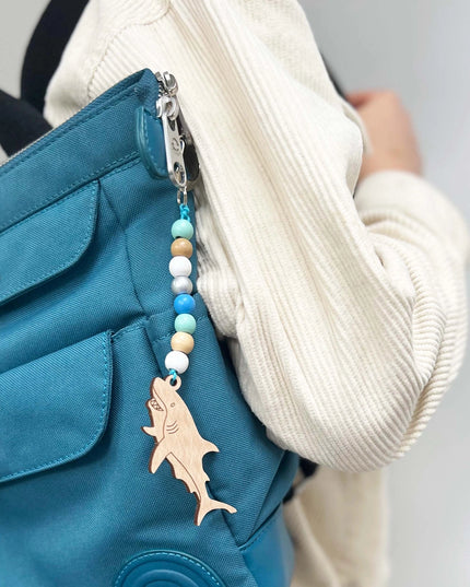 Blue bag with a shark charm and bead chain held by a person wearing a white sweater.