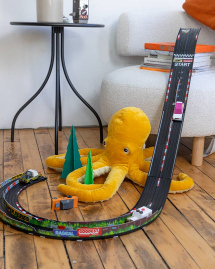 Toy race track set up with a plush octopus and small cars on a wooden floor.