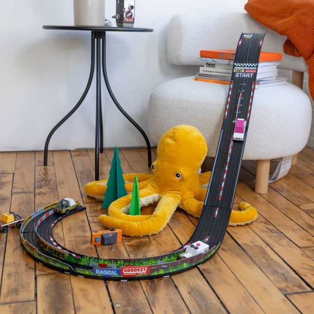 Toy race track set up with a plush octopus and small cars on a wooden floor.