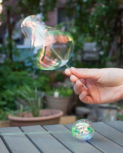 Hand holding a bubble wand with a bubble, set against a garden background