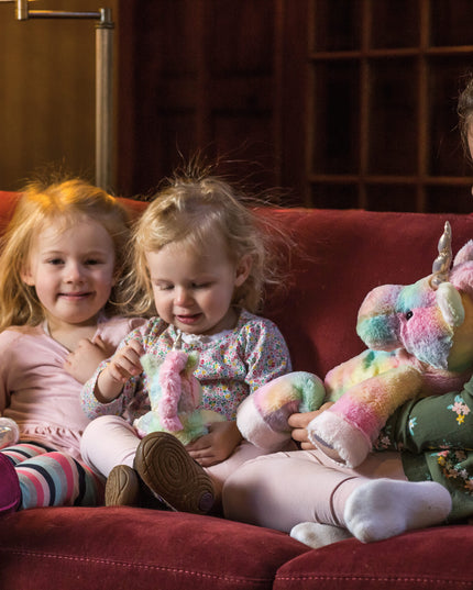 Three children sitting on a red couch with colorful stuffed toys.