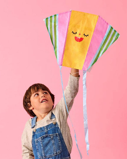 Child holding a colorful kite against a pink background