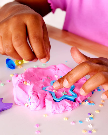Children playing with pink play dough and cookie cutters on a white surface.