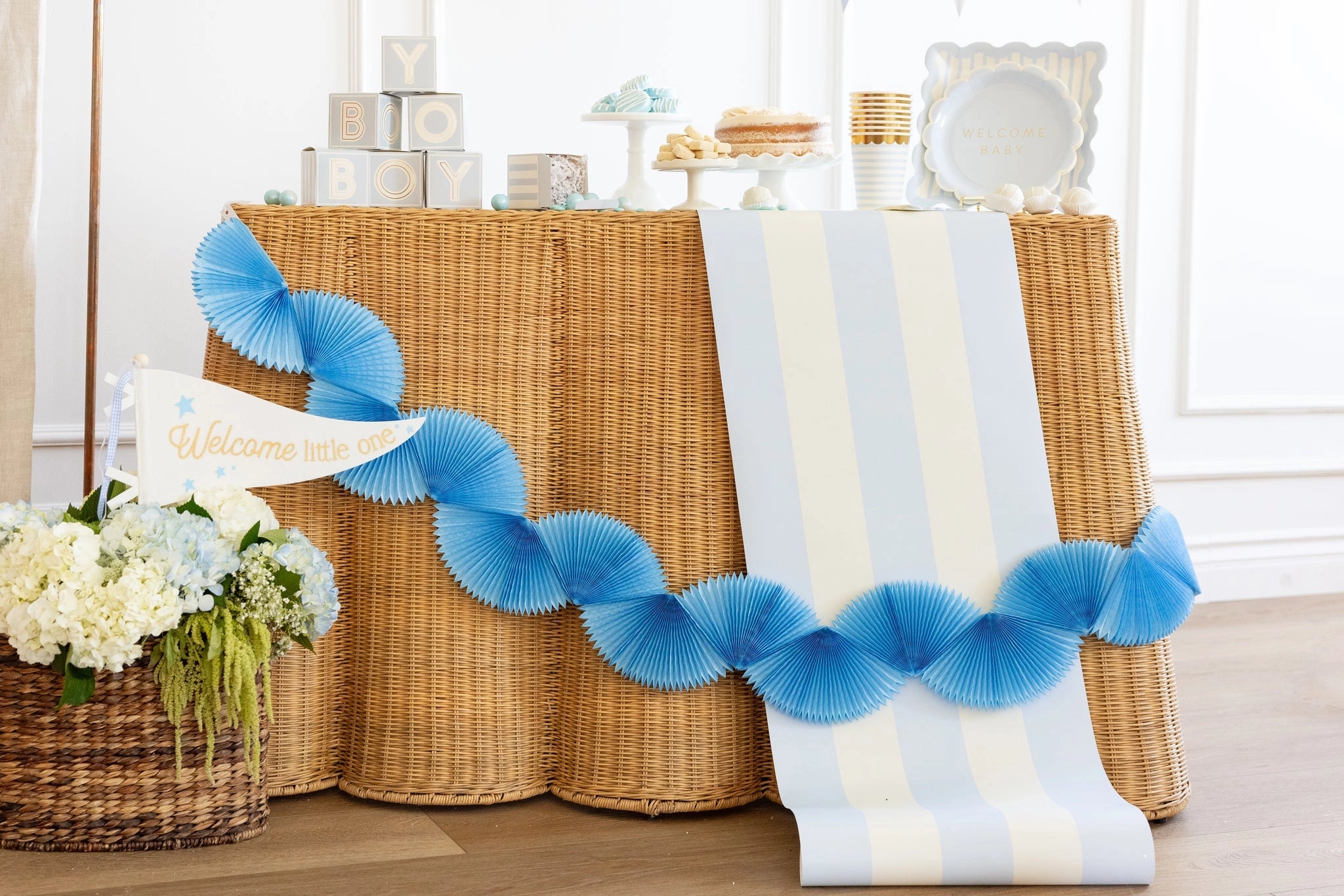 Decorative blue streamer with 'Welcome' sign on a table with floral arrangement and wicker baskets.