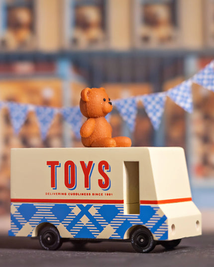 Toy truck with a teddy bear on top, set against a blurred background with bunting.