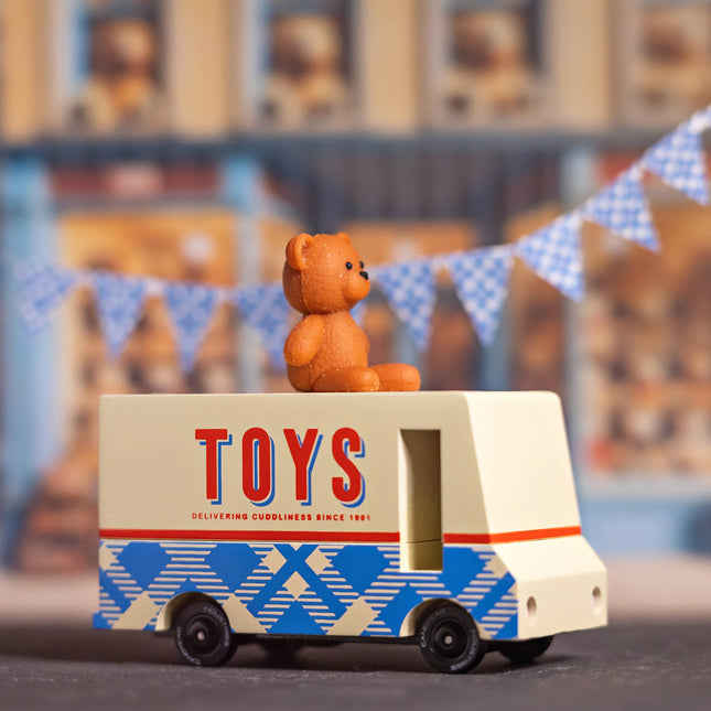 Toy truck with a teddy bear on top, set against a blurred background with bunting.