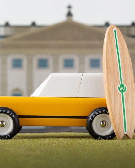 Toy car with a surfboard on grass in front of a building