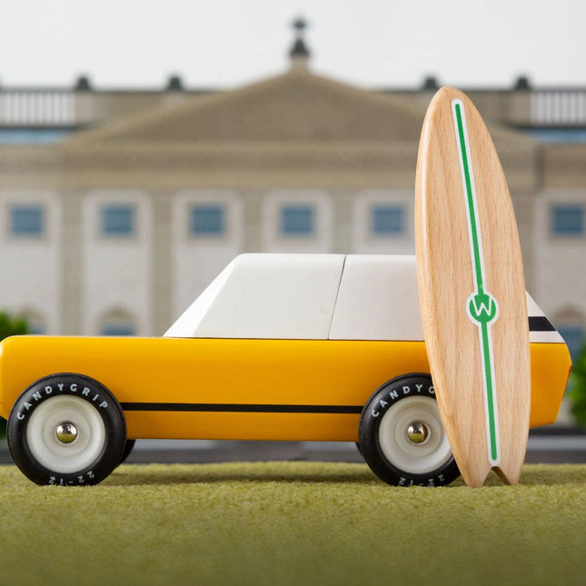 Toy car with a surfboard on grass in front of a building