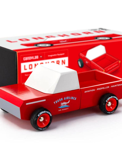 Red toy truck with white top, next to its packaging on a white background