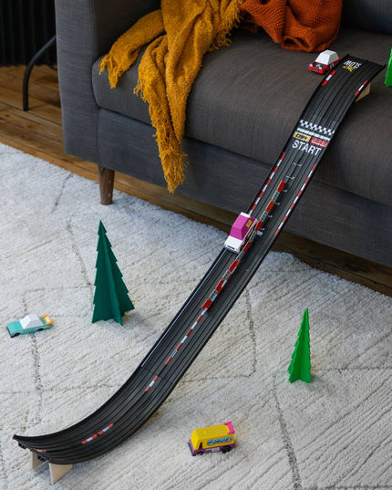 Toy race track with cars on a carpeted floor next to a sofa.