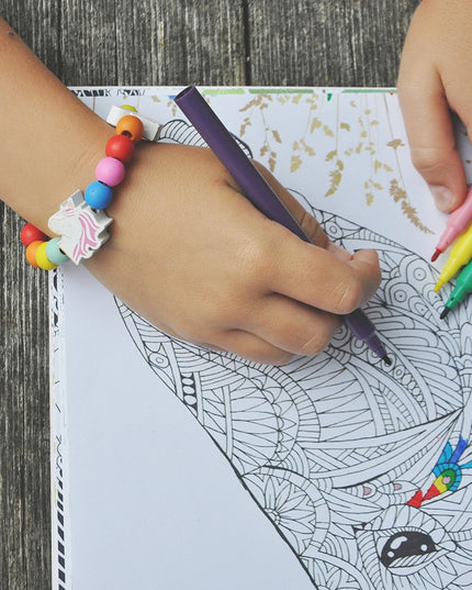 Child coloring a detailed design with colorful markers on a wooden surface