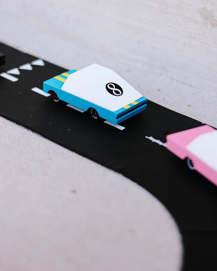 Model cars on a black road with white markings against a light gray background