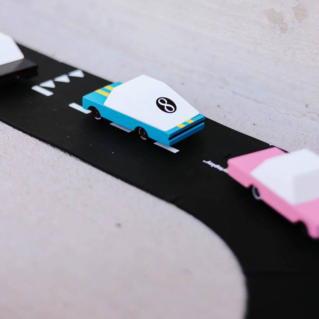 Model cars on a black road with white markings against a light gray background