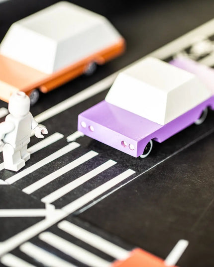 Small toy cars on a track with a white figure nearby