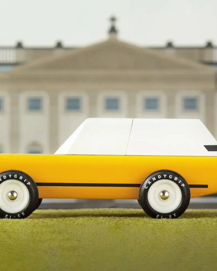 Yellow toy car with white top on grass in front of a building