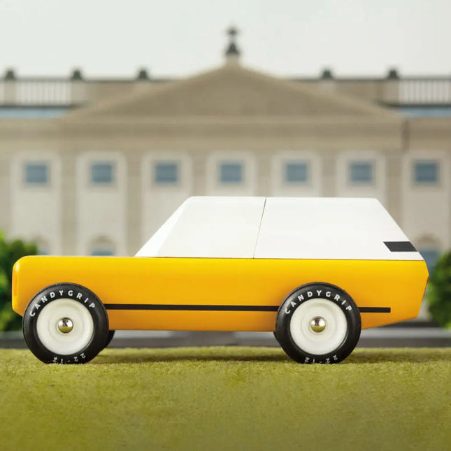 Yellow toy car with white top on grass in front of a building