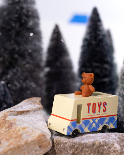 Toy truck with a teddy bear on top in a snowy landscape with miniature trees.
