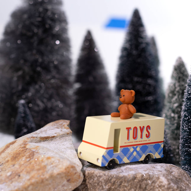 Toy truck with a teddy bear on top in a snowy landscape with miniature trees.