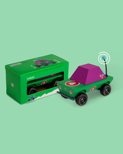 Toy car with purple roof and green body next to its packaging on a light green background