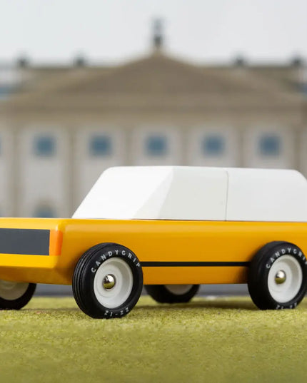 Yellow toy car with a white top on a grassy surface with a blurred building in the background