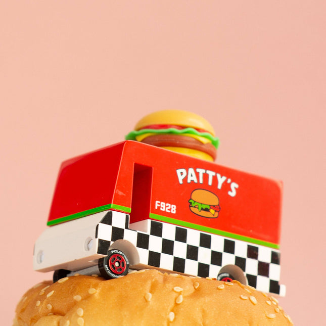 Toy truck labeled 'Patty's' with a hamburger on top of a burger bun against a pink background