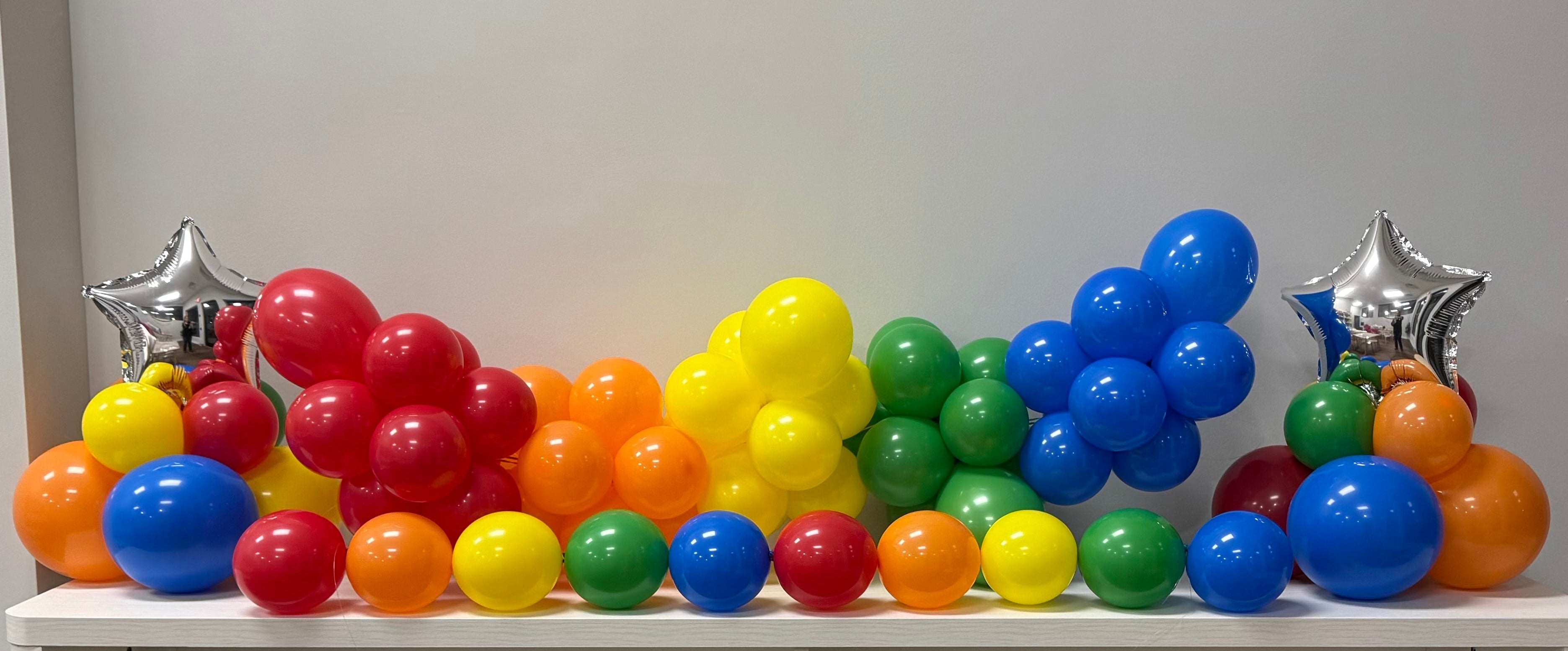 Colorful balloons arranged in a rainbow pattern on a white shelf with silver star decorations.