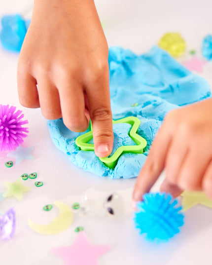 Children playing with blue play dough and green tools on a white surface.
