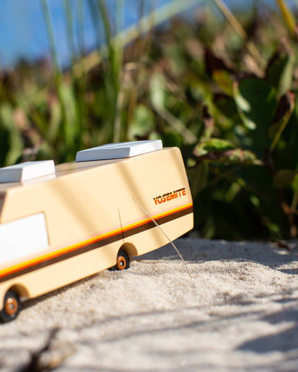 Wooden toy van on a sandy surface with greenery in the background
