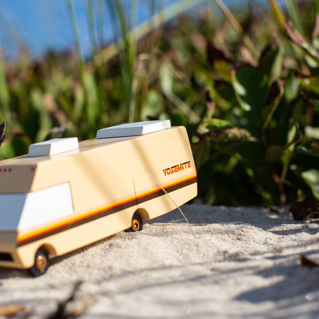 Wooden toy van on a sandy surface with greenery in the background