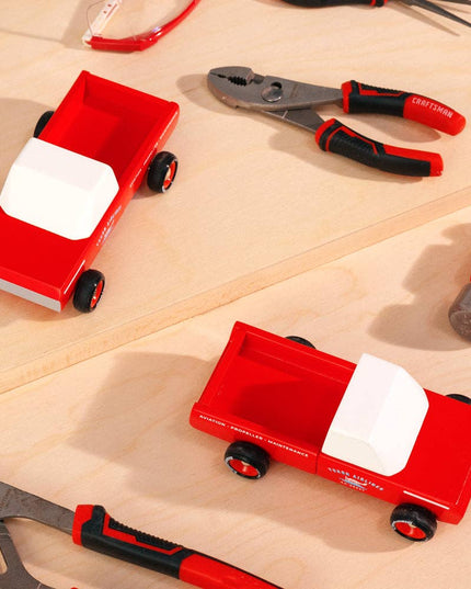 Red toy trucks with white beds on a wooden surface surrounded by tools.