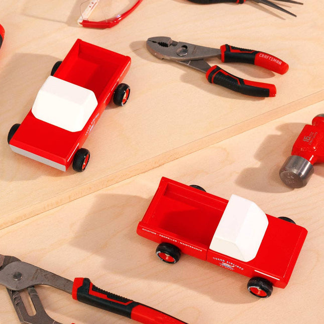 Red toy trucks with white beds on a wooden surface surrounded by tools.