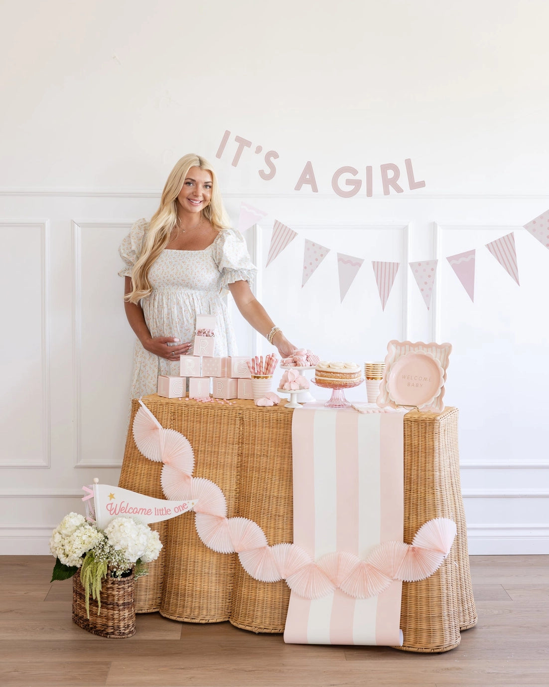 Pregnant woman standing behind a decorated table with 'It's a Girl' banner.