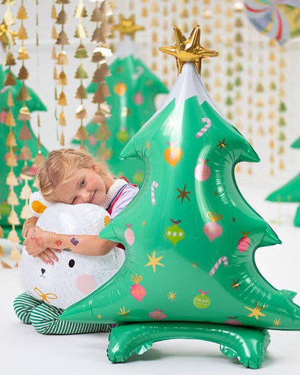 Child hugging a large inflatable green Christmas tree with a star on top, surrounded by festive decorations.