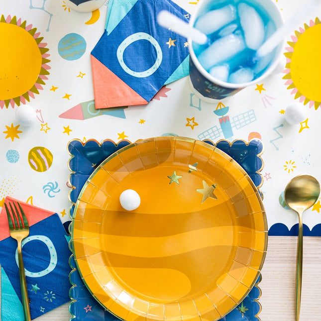 Yellow paper plate with a white ball on a colorful table setting with cups, napkins, and utensils.