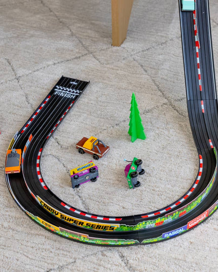 Toy race track set up on a grey carpet floor with toy cars and a tree.