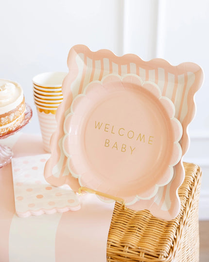 Pink decorative plate with 'Welcome Baby' text in a wicker basket on a light background