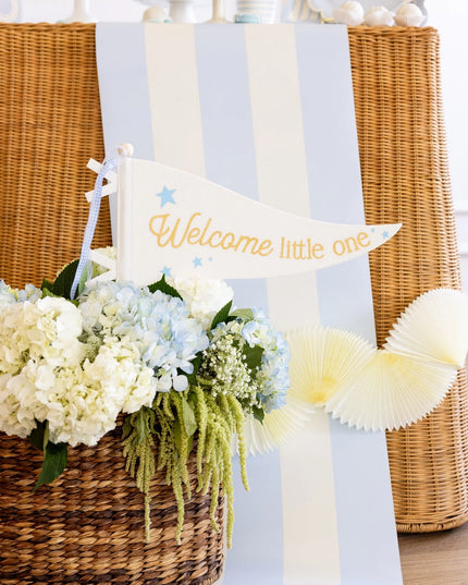 Decorative setup with flowers, a basket, and a 'Welcome little one' sign on a light blue background.