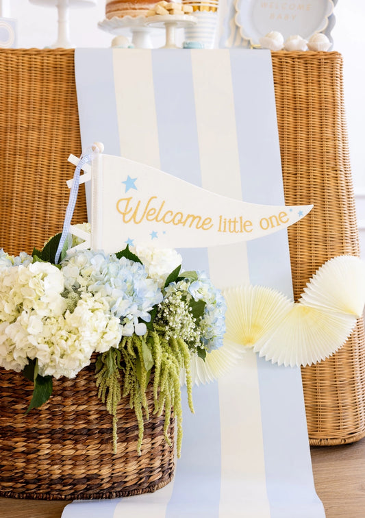 Decorative setup with flowers, a basket, and a 'Welcome little one' sign on a light blue background.