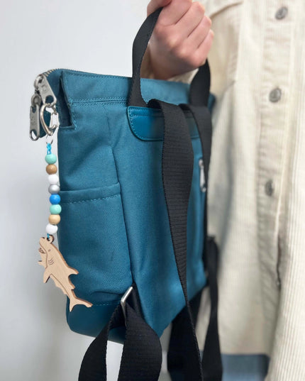Blue bag with a shark keychain attached, held by a person wearing a beige jacket.
