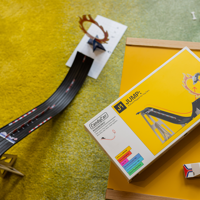 Model train track set with a box labeled 'Jump' on a yellow surface.