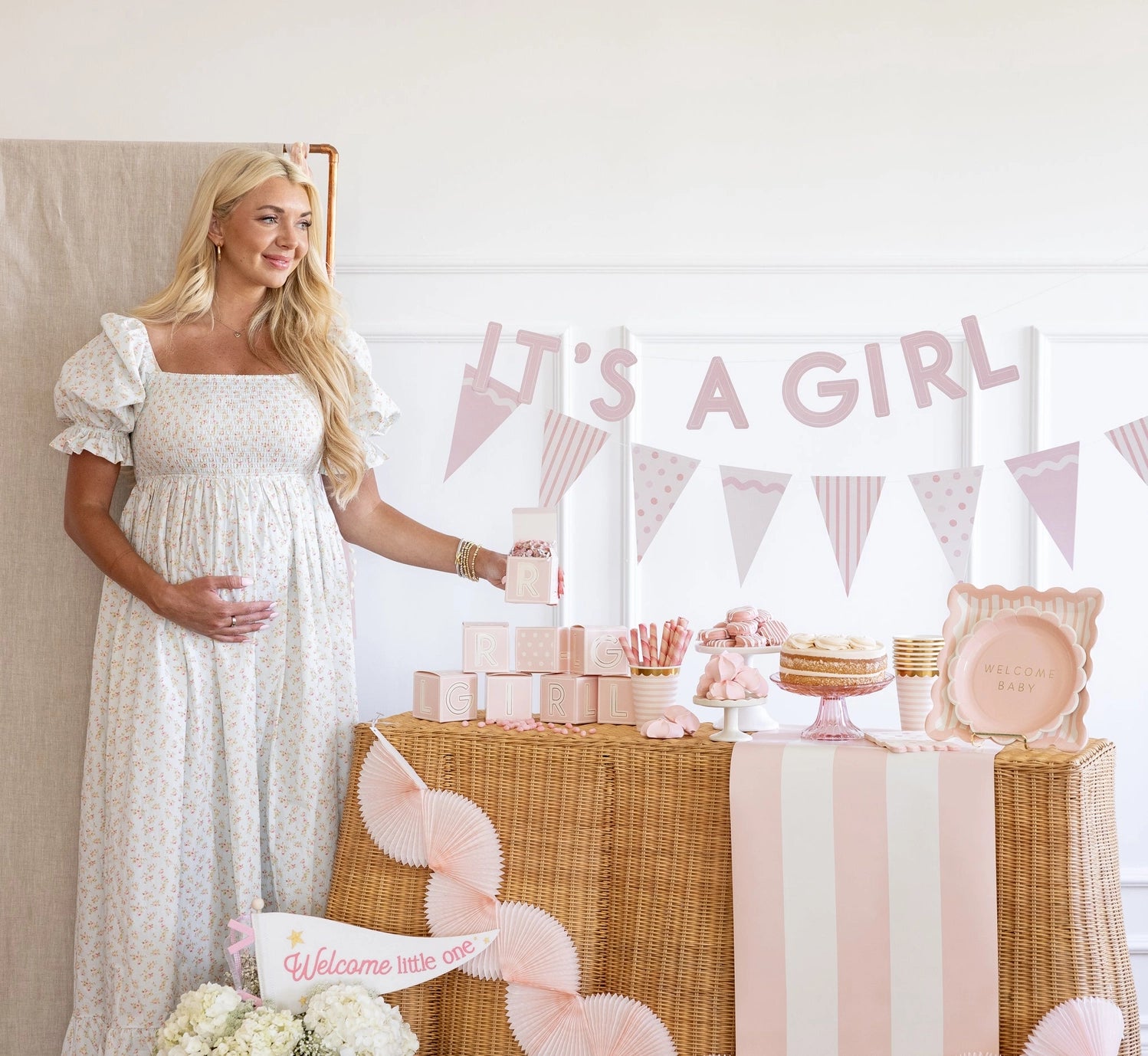 Pregnant woman standing next to a baby shower setup with 'It's a Girl' banner.